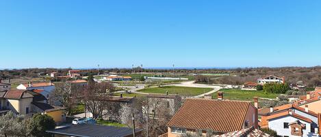 A residential area with terracotta-roofed houses, a sports field, and a clear blue sky.