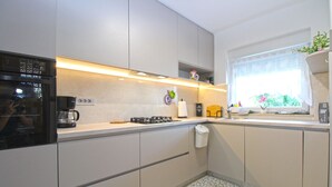 Ett modernt kök med en inbyggd ugn, en kaffebryggare och ett fönster med utsikt över grönområden.