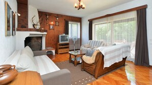 Ein gemütliches Wohnzimmer mit Kamin, Fernseher, einer Couch und einem großen Fenster mit Spitzenvorhängen.
