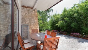 Eine überdachte Terrasse mit einer Steinmauer, einem runden Tisch, Holzstühlen und einer Glaseinfassung.
