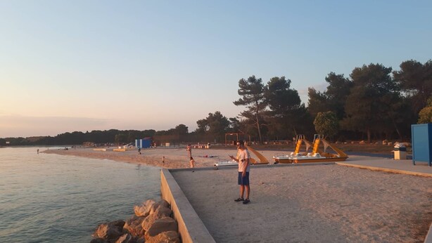 Een strand met een betonnen pad, een zandgebied en enkele mensen.