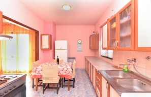 A compact kitchen with a dining table, chairs, a refrigerator, a sink, and cabinets.