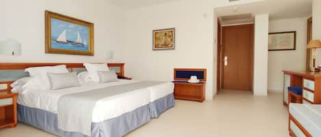 A hotel room with a large bed, a wooden nightstand, a desk with a chair, and a door leading to another room.
