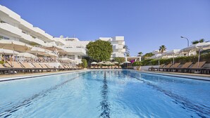 Une grande piscine entourée de bâtiments blancs dotés de balcons, avec des chaises longues et des parasols à proximité.