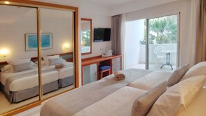 Une chambre d’hôtel avec deux lits, un bureau avec une chaise, une télévision et un balcon donnant sur des palmiers.