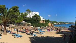 Une plage avec des transats, des parasols et un bâtiment en arrière-plan.
