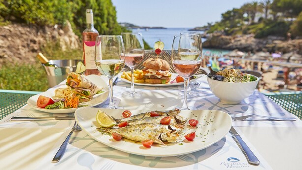 Une table dressée avec de la nourriture et des boissons, donnant sur une plage.