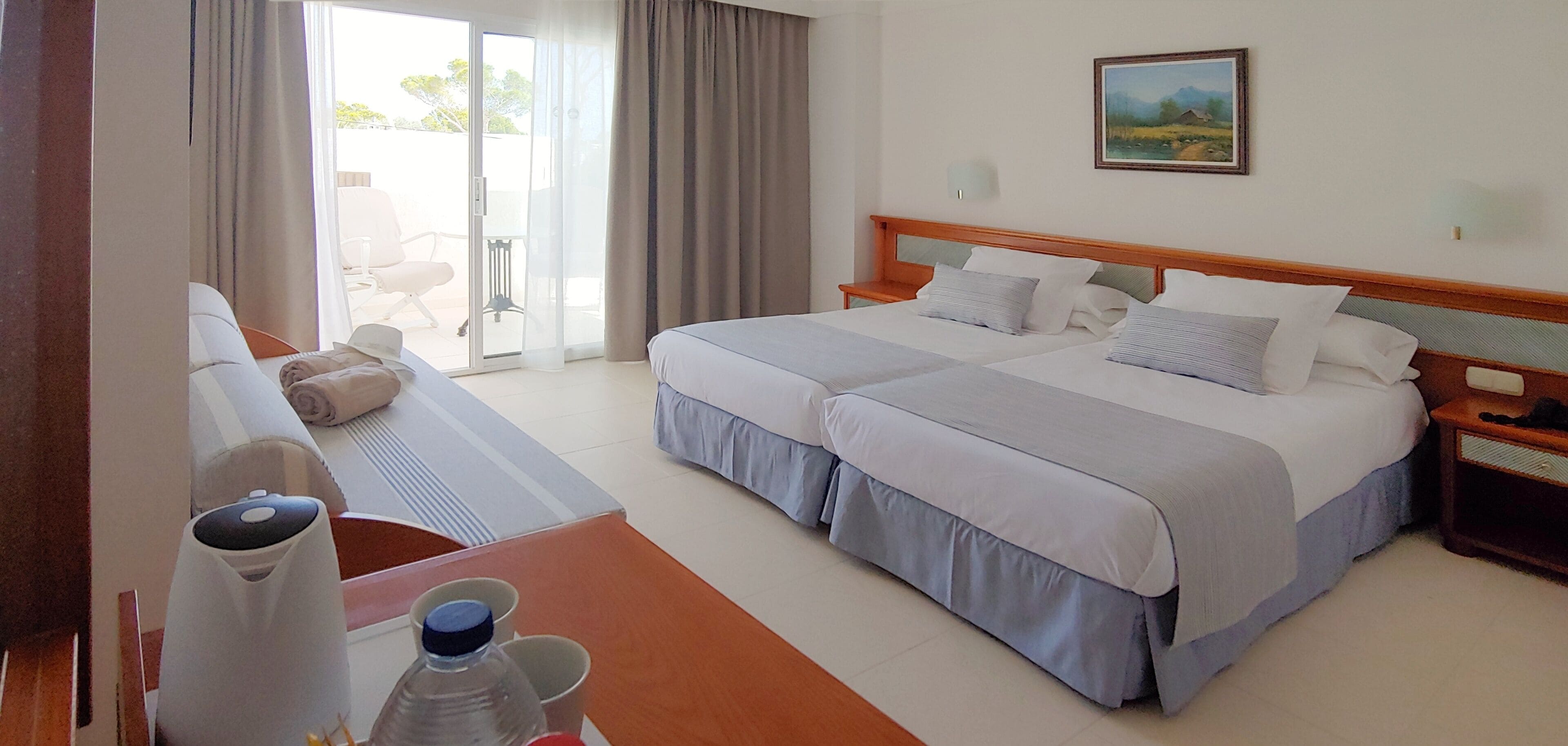 Ein Hotelzimmer mit zwei Betten, einem Sofa, einem Tisch mit Flasche und Tasse sowie einem Bild an der Wand.