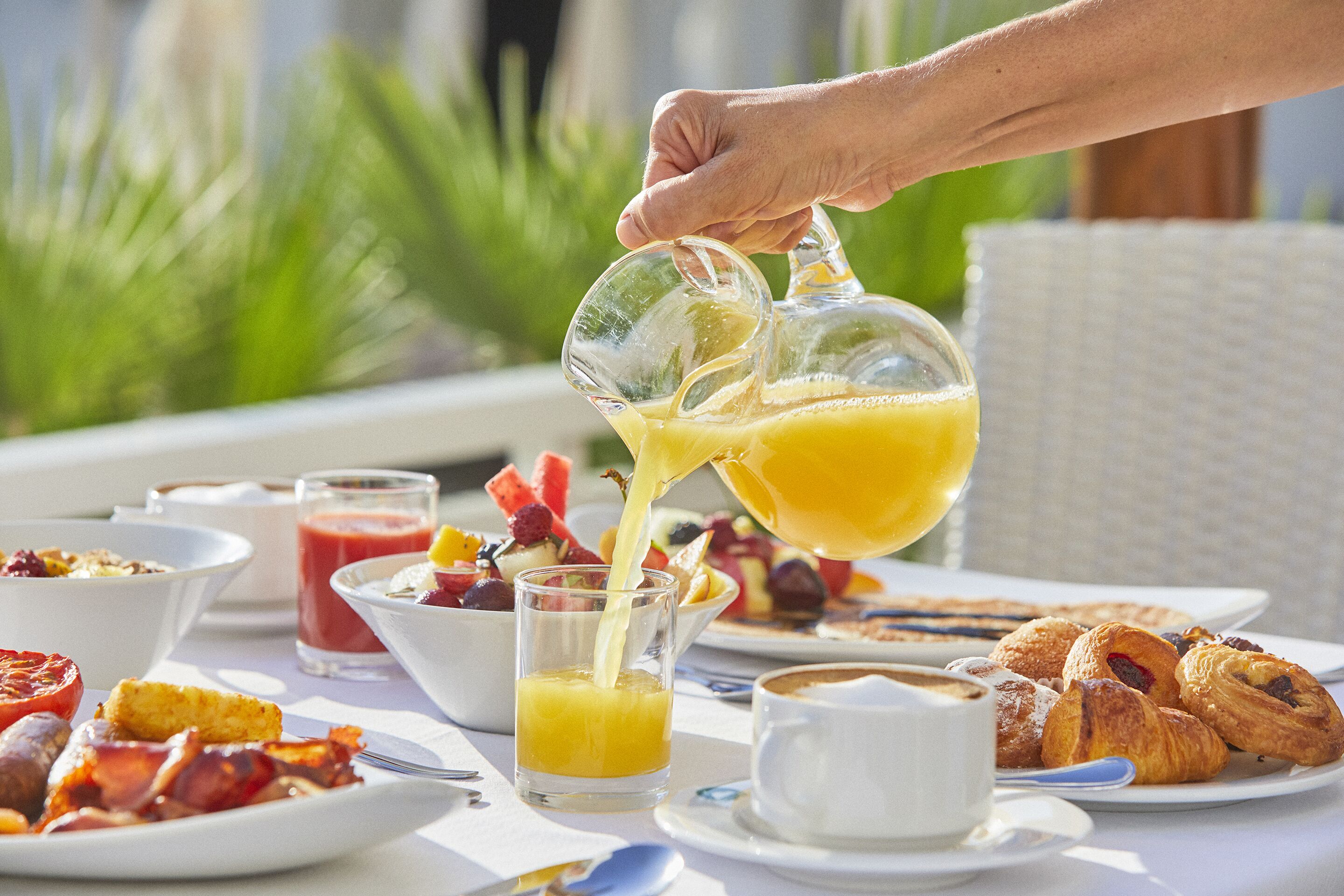 Een ontbijttafel met diverse gerechten, waaronder een glas jus d'orange, een fruitsalade en gebak.