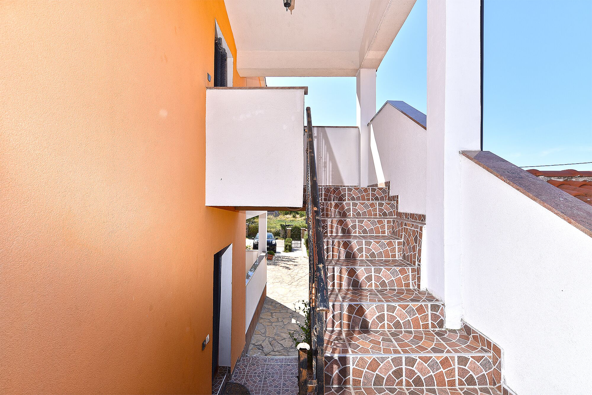 Un étroit couloir extérieur menant à un escalier dont les marches sont recouvertes de carreaux décoratifs.