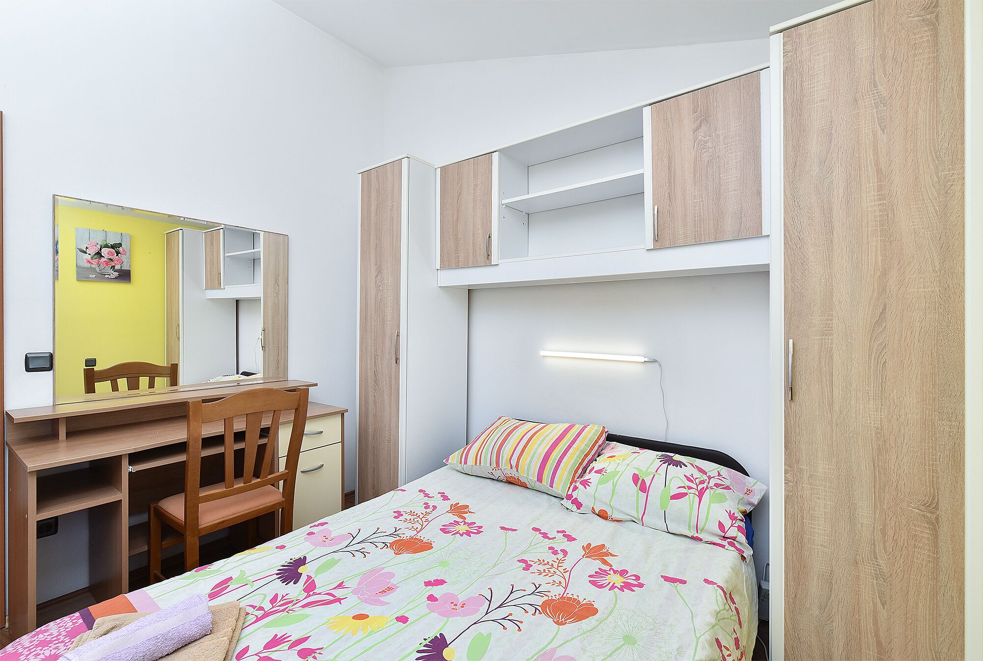 A bedroom with a bed, a desk, a chair, and a wardrobe.