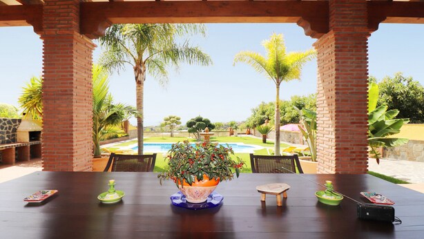 A covered patio with a pool view, a table with a potted plant, and outdoor seating. - 1128 Villa AndreaSol (Frigiliana)
