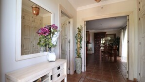 A hallway with a white console table, a mirror, and a vase with flowers. There is a door leading to another room with a dining table and chairs. - 1128 Villa AndreaSol (Frigiliana)