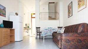 Un espacio habitable compacto con sofá, televisor, refrigerador y comedor con sillas y mesa.
