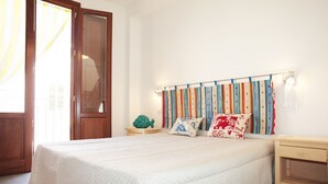 Un dormitorio con cama, una mesita de noche de madera, una pequeña mesa y una cortina colorida.