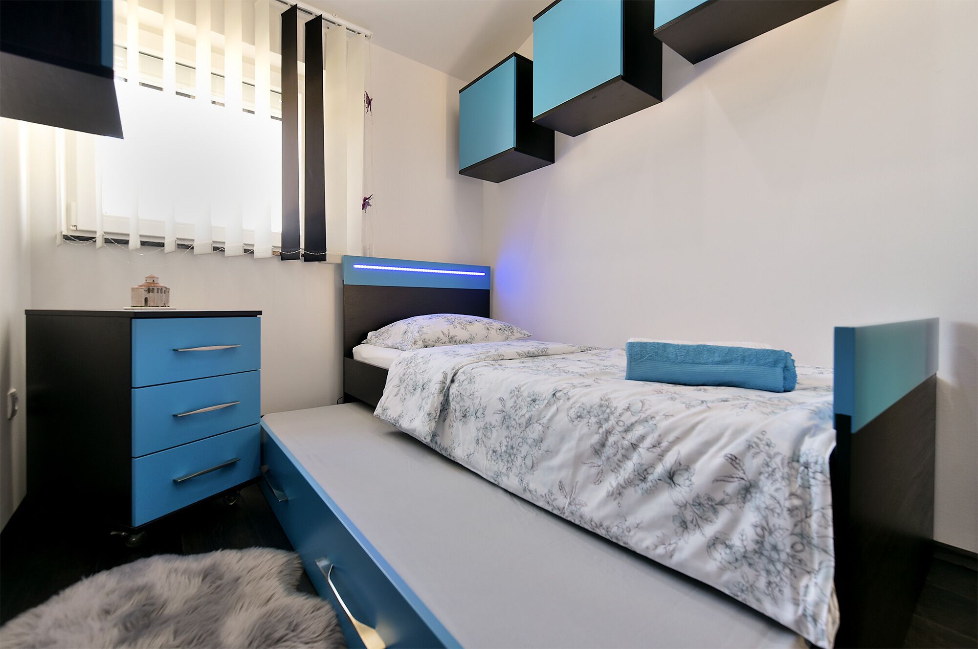 A bedroom with a bed, a dresser, and a window with blinds.