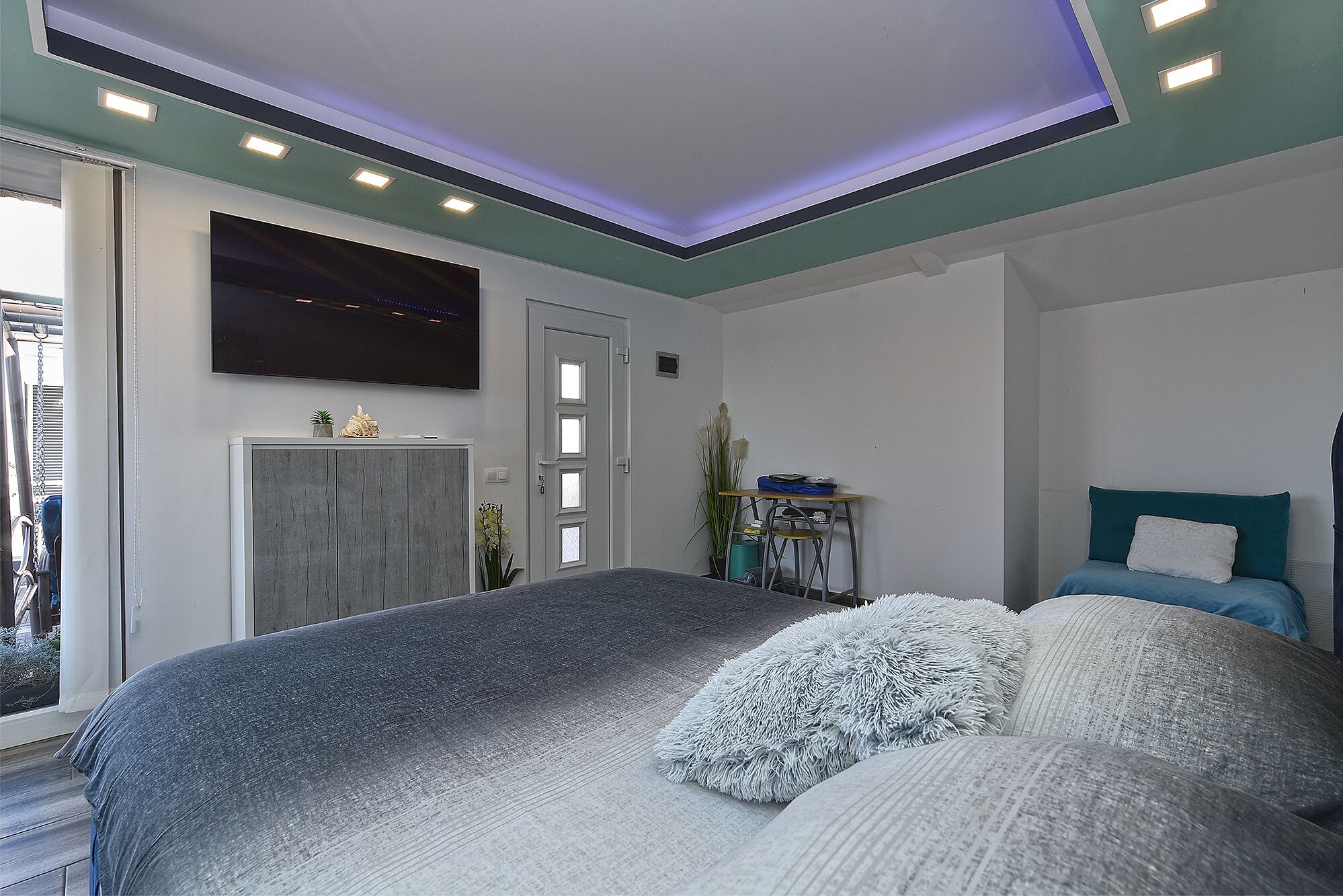 Ein modernes Schlafzimmer mit einem großen Bett, einem an der Wand montierten Fernseher und einem kleinen Schreibtisch mit Stuhl.