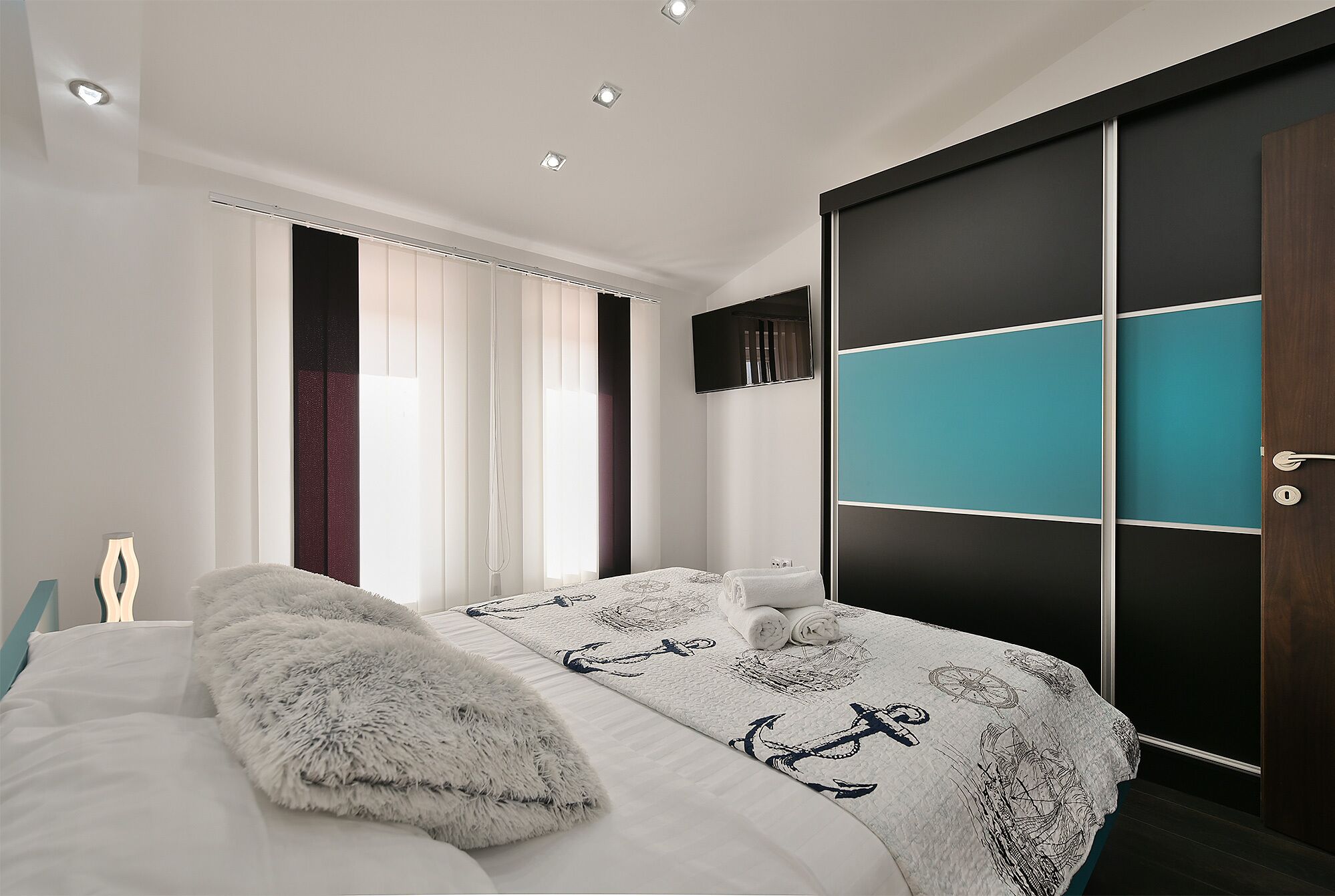 A modern bedroom with a bed, a fluffy pillow, a window with curtains, and a wardrobe with teal accents.