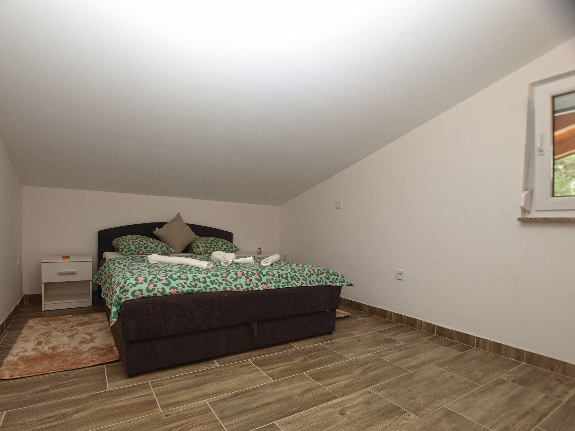 Un dormitorio con cama, mesita de noche y ventana.