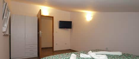 A hotel room with a bed, a wardrobe, a television, and a door leading to another room.