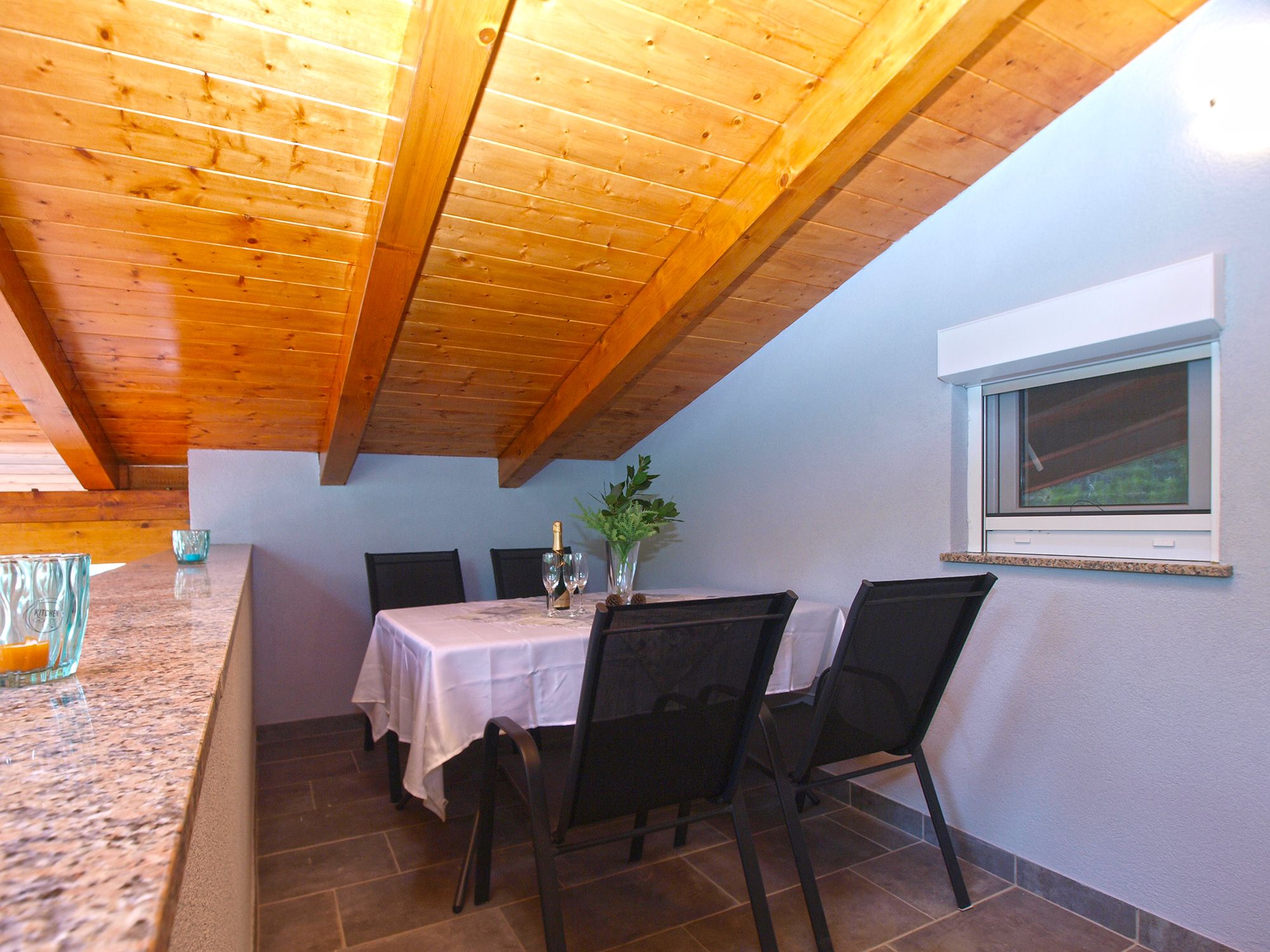 A dining area with a table set for two, wooden ceiling beams, and a window with a view.