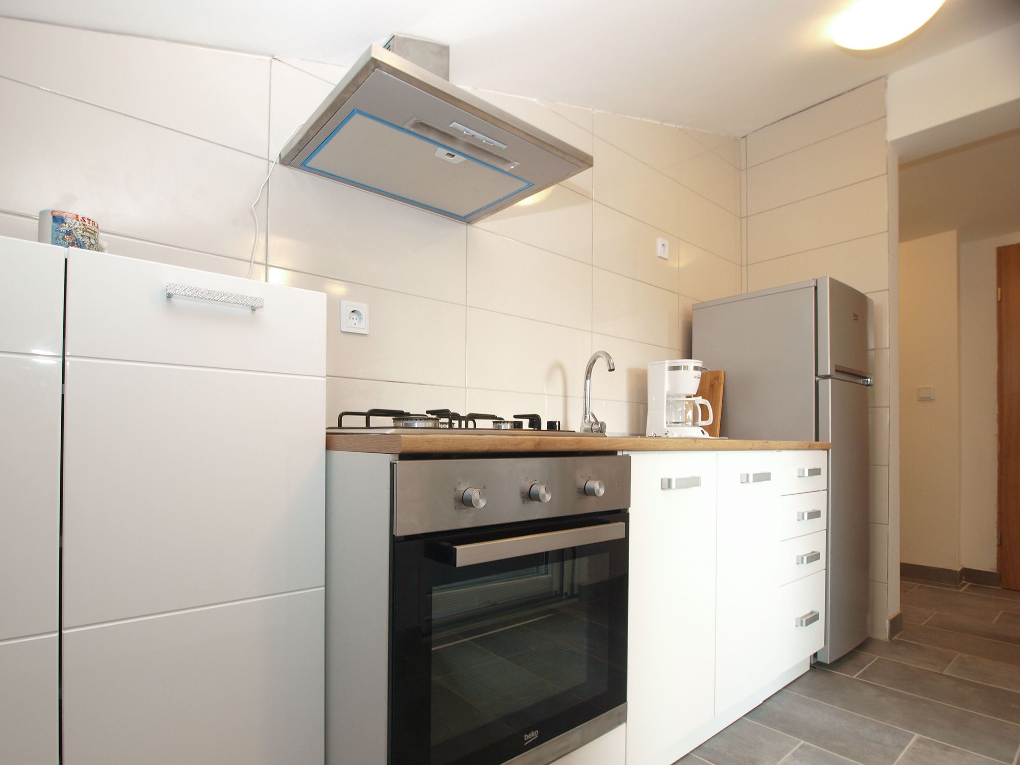 A modern kitchen with white cabinetry, a built-in oven, a gas stove, and a coffee maker on the countertop.