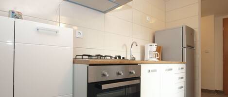 A modern kitchen with white cabinetry, a built-in oven, a gas stove, and a coffee maker on the countertop.