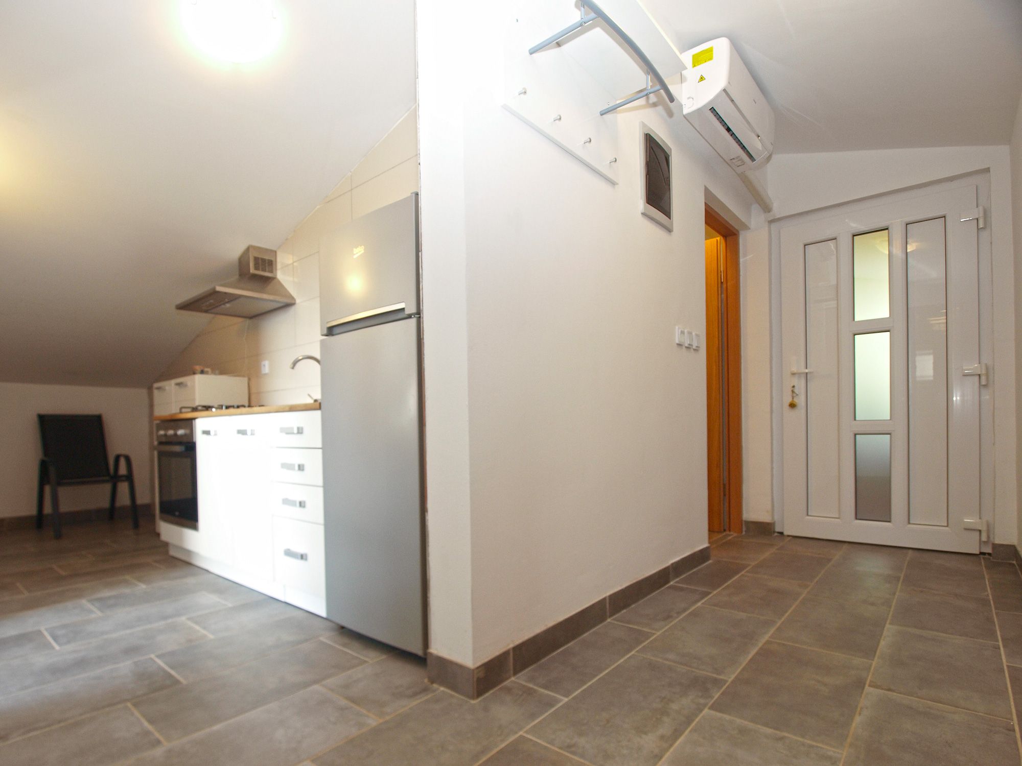A modern kitchen with a built-in oven, a refrigerator, and a wall-mounted air conditioning unit.