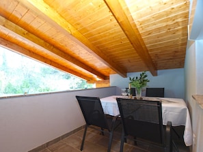 Ein Essbereich mit einem Tisch für zwei Personen, Holzbalkendecke und ein Fenster mit Blick auf Grünflächen.