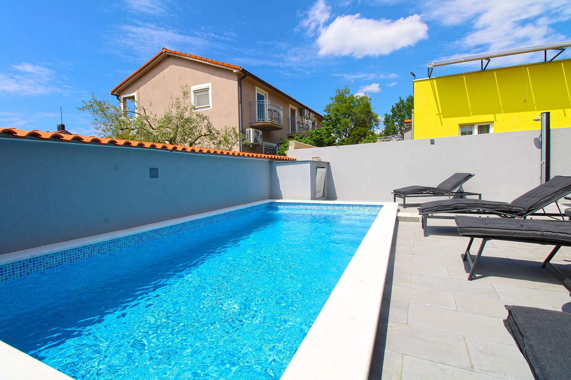 Una piscina con sillas de descanso, un deck con baldosas y un edificio con techo de tejas.