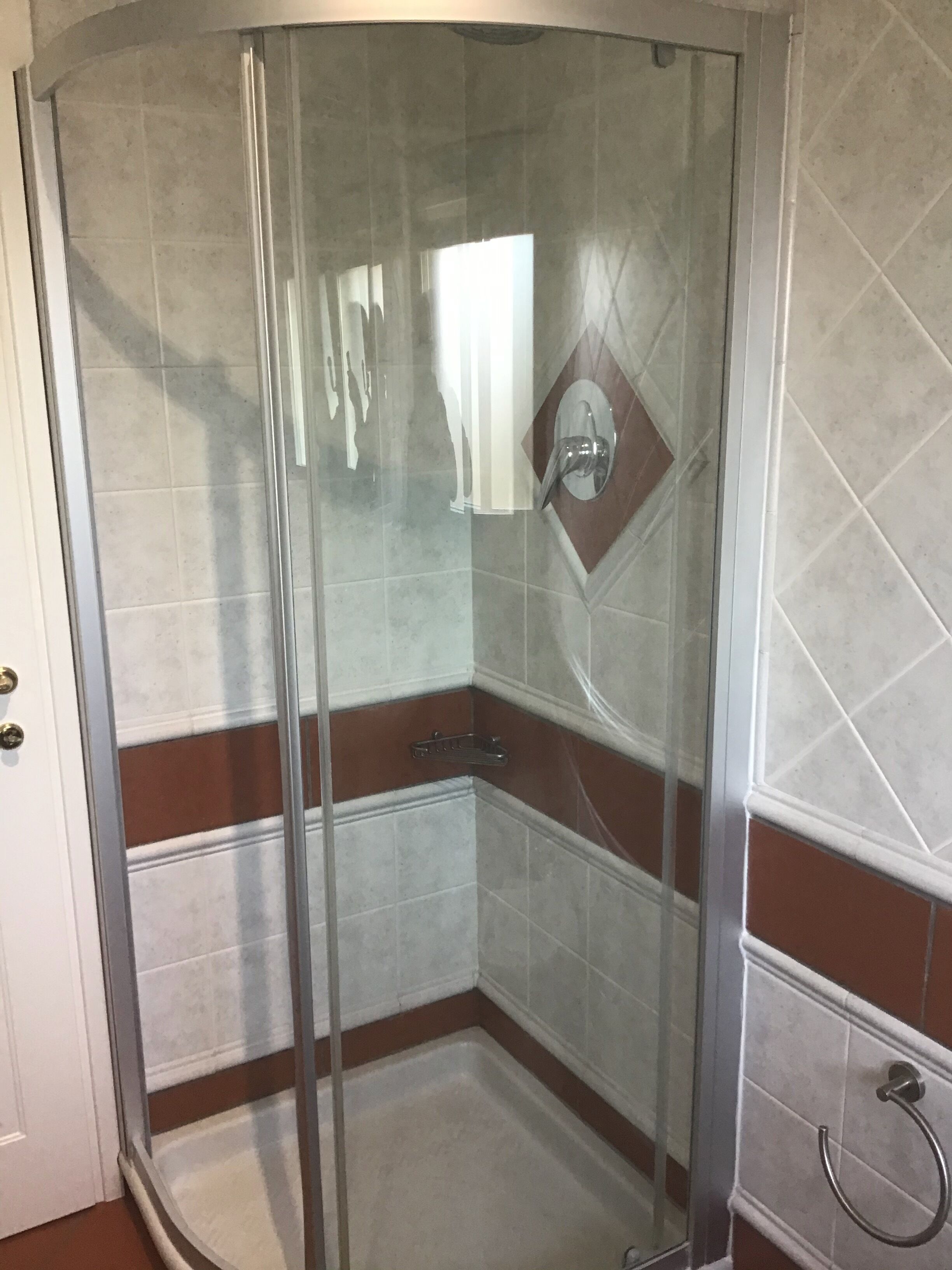 A glass-enclosed shower with a corner design, a wall-mounted faucet, and a towel ring.