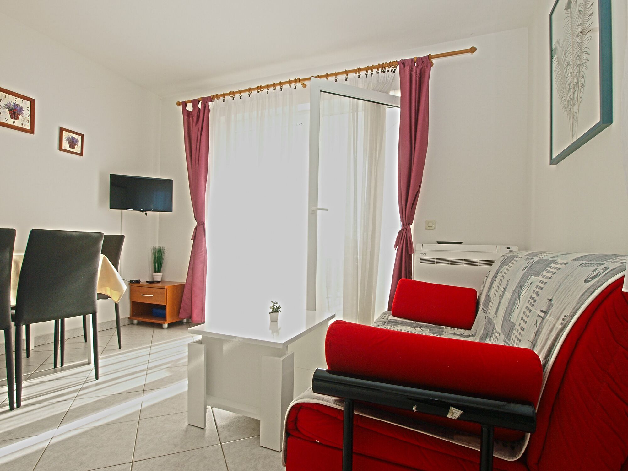 Una sala de estar moderna con un sofá rojo, una mesa de centro blanca, un televisor y un comedor con sillas y una mesa.