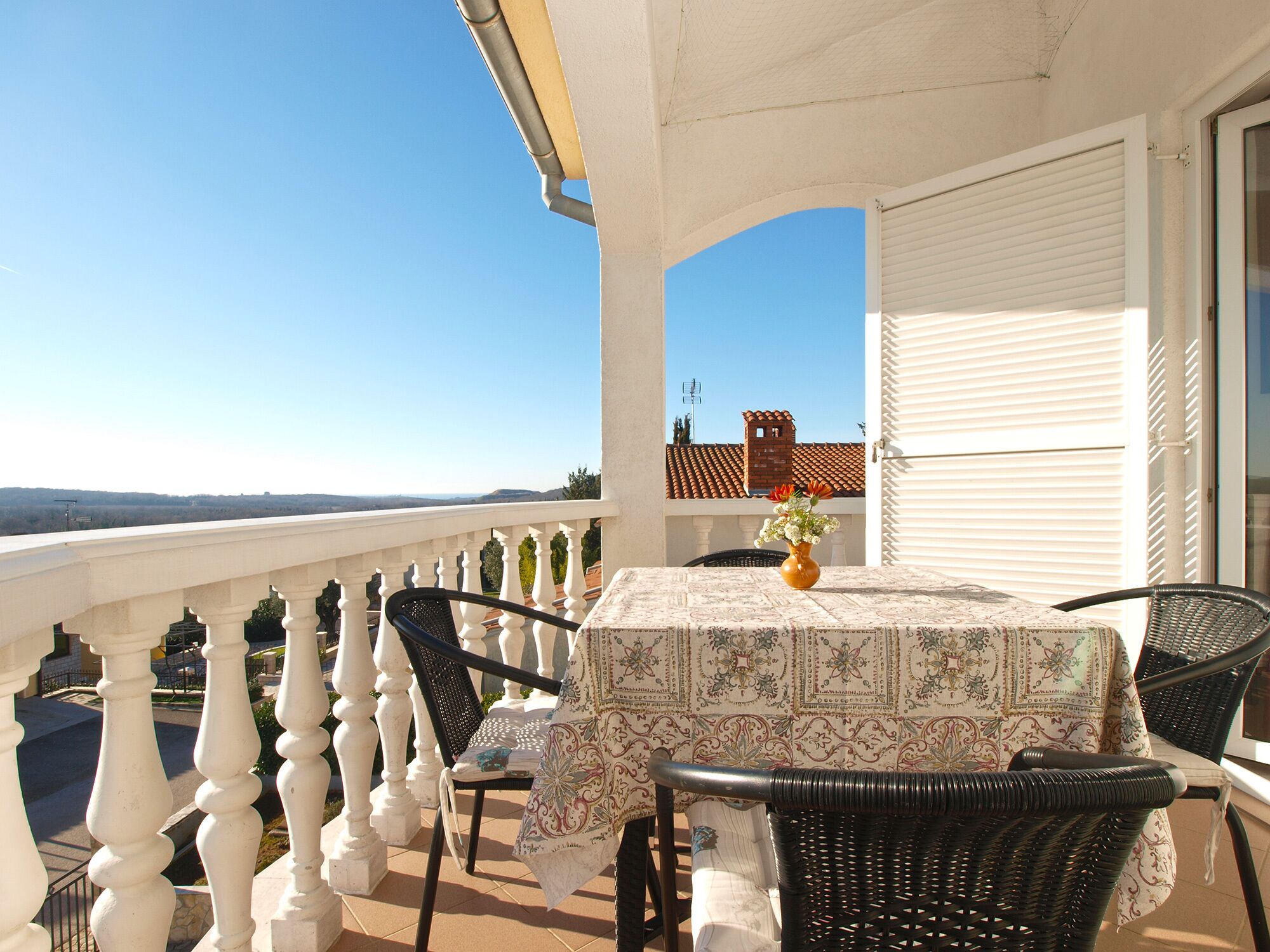 Ein Balkon mit Tisch und Stühlen, einer Blumenvase und Blick auf die Landschaft.