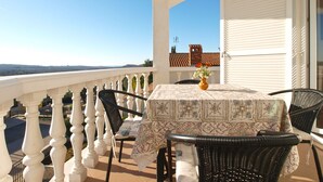 Ein Balkon mit Tisch und Stühlen, einer Blumenvase und Blick auf die Landschaft.