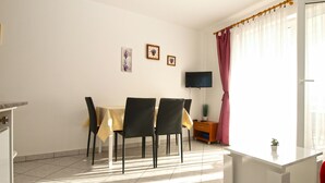 Ein Essbereich mit Tisch und Stühlen, einem Fernseher an der Wand und einem Fenster mit Vorhängen.