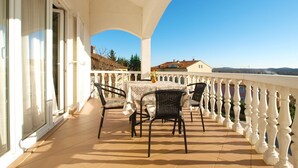 A balcony with a table and chairs, a white railing, and a view of buildings and hills in the distance. - Apartment 1978/26796 (Istria - Poreč), 5000m from the beach (Porec)