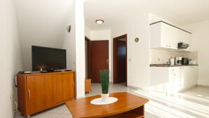A modern living room with a wooden cabinet, a television, a small table with a plant, and a kitchen area with cabinets and appliances. - Apartment 1978/26796 (Istria - Poreč), 5000m from the beach (Porec)