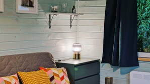 Ett mysigt rum med en soffa, kuddar, ett sängbord med en lampa och ett litet sidobord.