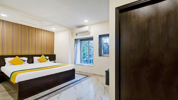 Una habitación de hotel con cama, cabecero de madera, ventana con barrotes y un equipo de aire acondicionado.