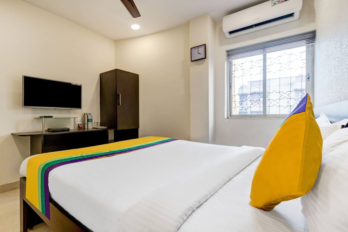 Une chambre d’hôtel équipée d’un lit, d’une télévision, d’une armoire, d’une fenêtre avec des barreaux et d’un appareil de climatisation.