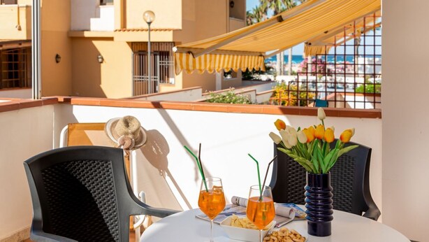 A balcony with a table set for two, featuring drinks, a vase of tulips, and a plate of snacks. - I Tre Golfi Faro Blu Apartment (San Vito Lo Capo)