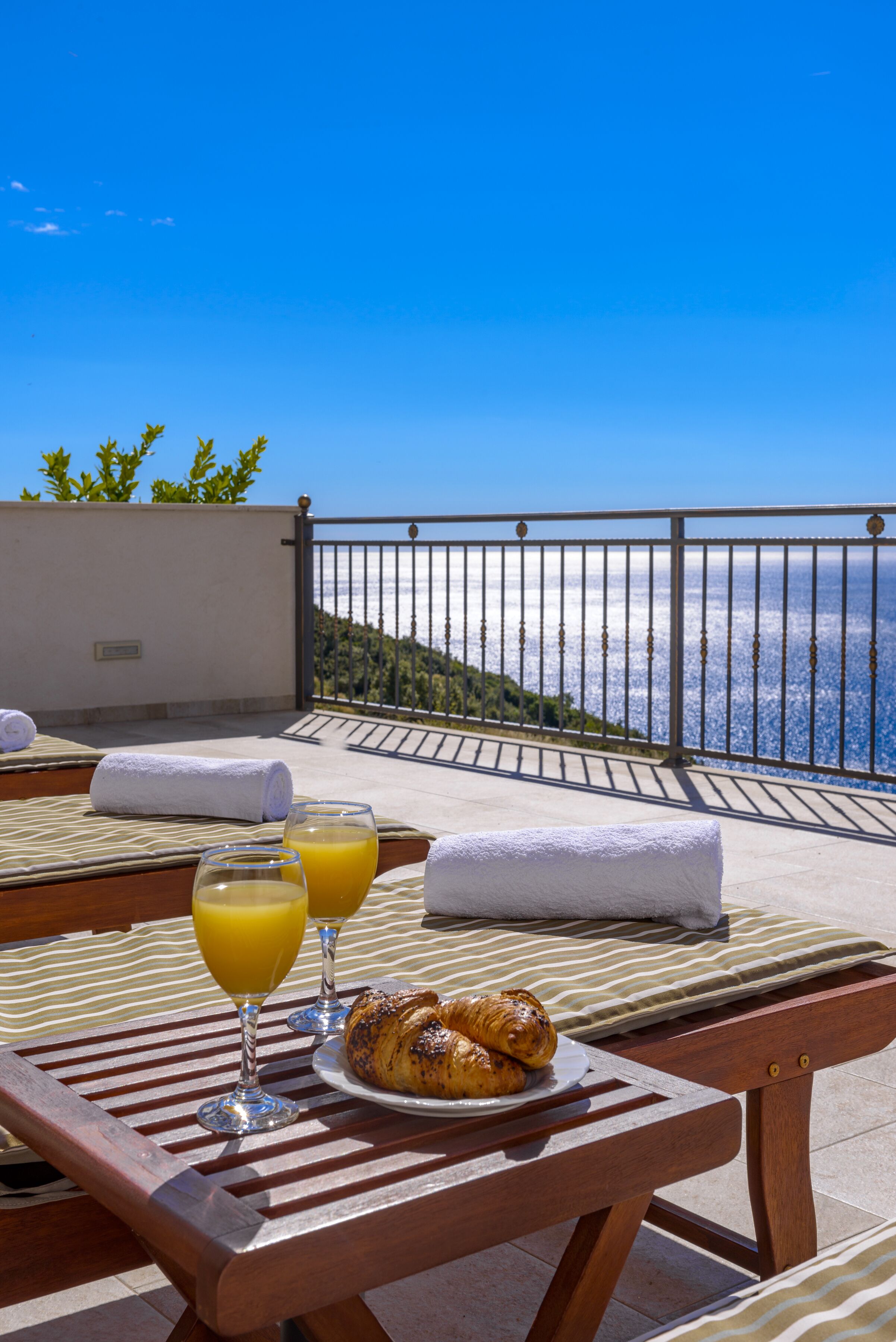 Ein Balkon mit Frühstückstisch, ausgestattet mit Croissants und Orangensaft, mit Blick auf eine schöne Aussicht.