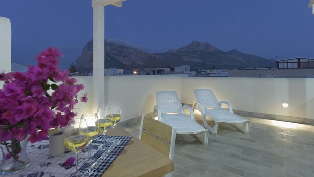 Eine Terrasse mit einem Tisch für zwei Personen, zwei weißen Liegestühlen und einer Vase mit rosa Blumen.
