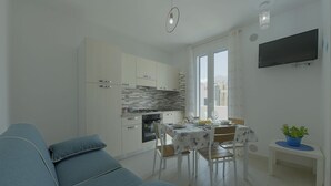 Eine moderne Küche mit weißen Schränken, einem Esstisch mit Stühlen, einem blauen Sofa und einem kleinen Tisch mit einer Pflanze.