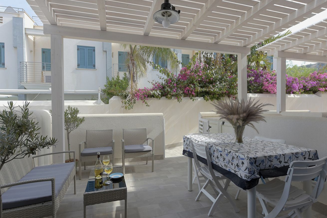 Eine Terrasss mit Korbmöbeln, einem Tisch mit gemustertem Tischläufer und Kübelpflanzen.