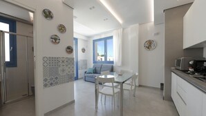 Eine moderne Küche mit weißen Schränken, einem Esstisch mit Stühlen und Blick auf den Wohnbereich mit einer Couch und blauen Vorhängen.