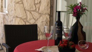 A table with a red tablecloth, two wine glasses, a bottle of wine, a bowl of strawberries, and a vase with flowers. - Fox Apartments (Konavle)