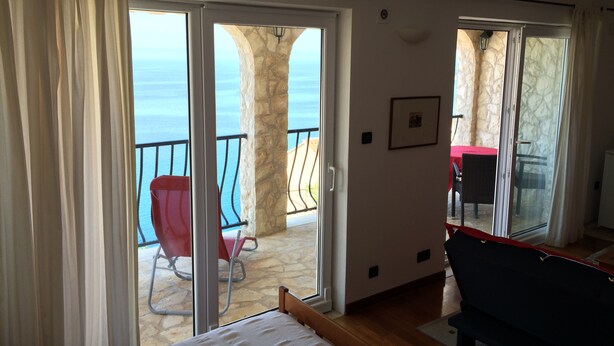 A bedroom with a large sliding glass door leading to a balcony with a stone pillar and a red chair. - Fox Apartments (Konavle)