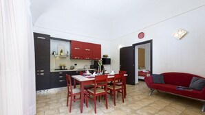 Un ambiente compatto con angolo ristoro, angolo cottura e divano rosso.