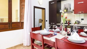 Zona pranzo con tavolo imbandito per quattro persone, sedie rosse e angolo cottura con elettrodomestici e pensili moderni.